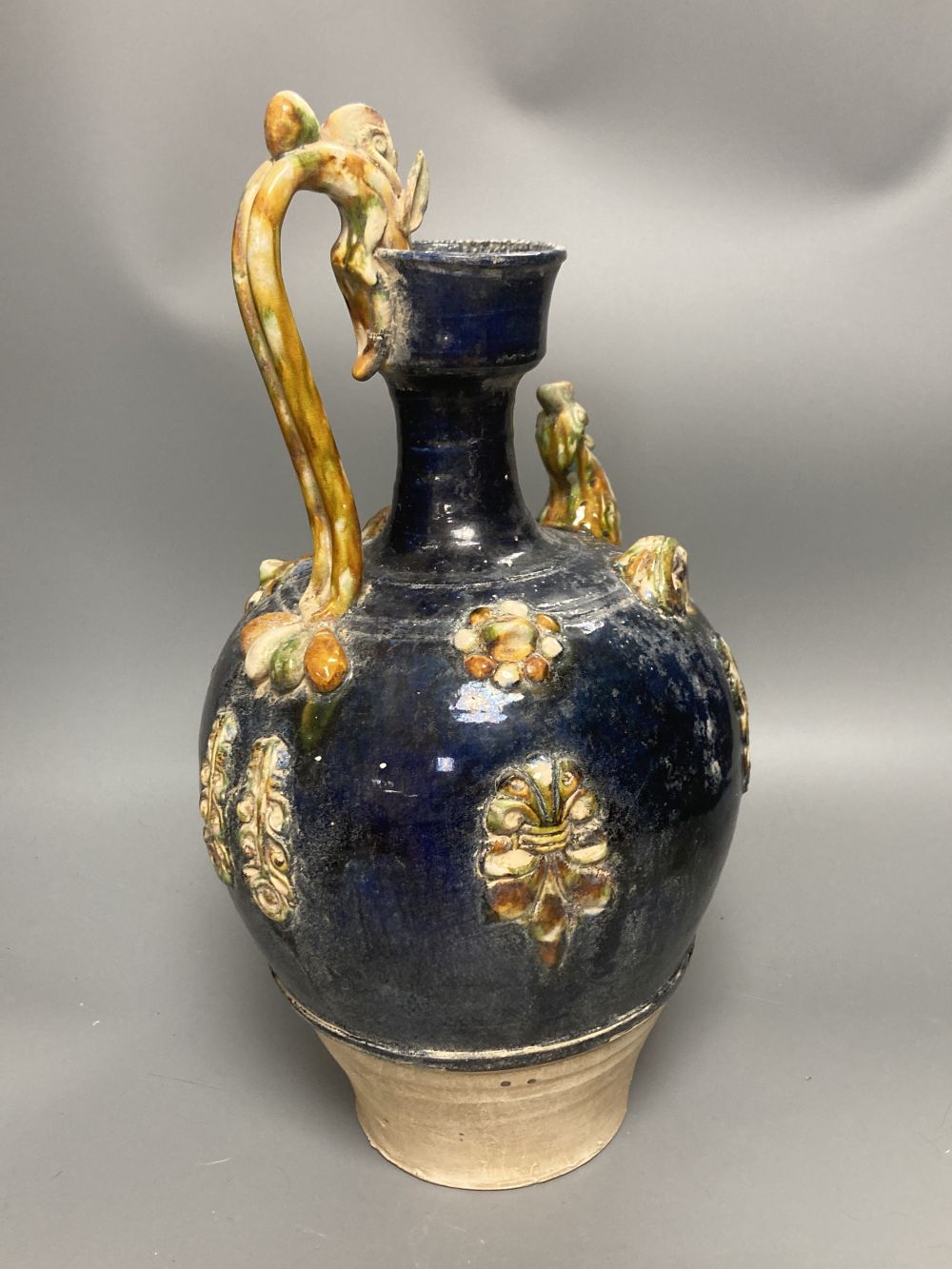 A group of Chinese Tang style pottery figures, tallest 28cm and a partially glazed ewer in sancai colours against a blue ground, 40cm